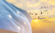 Waving flag of Micronesia against the background of a sunset or sunrise. Micronesia flag for Independence Day. The symbol of the state on wavy fabric.