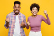 Young couple two friends family man woman of African American ethnicity wear purple casual clothes together do winner gesture celebrate clench fists say yes isolated on plain yellow orange background
