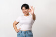 The cheerful young Asian woman smiling and showing the OK hand sign standing on white background.