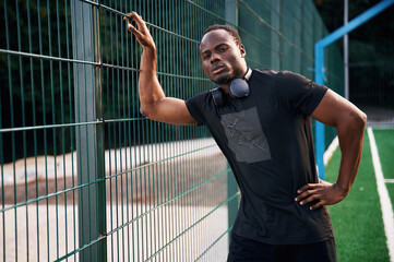 Wall Mural - With headphones on the neck. Handsome black man is posing outdoors at daytime