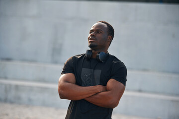 Wall Mural - Standing with arms crossed. Handsome black man is posing outdoors at daytime