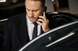 good looking red haired businessman in elegant stylish attire talking by mobile phone on parking lot