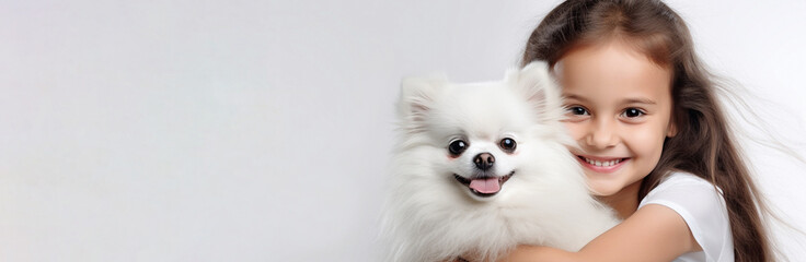 A smiling girl with long hair holds a fluffy white Pomeranian puppy on a gray monochrome background. A banner with space for text. The concept of caring for pets