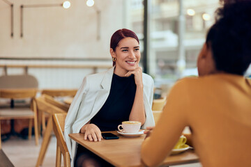 A pretty smiling woman talking with her female friends, drinking coffee, sitting at the cafe.