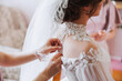 Morning of the bride. The bride's maid of honor helps the bride lace up her dress, fasten buttons on the dress or sleeves. Girlfriends help the bride fasten her dress