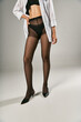 © LIGHTFIELD STUDIOS - partial view of model in white shirt and black pantyhose standing with hand on hip, grey background
