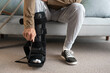 Young Man attaching an ankle orthosis to his leg to support ligaments while sitting on the sofa at home. Medicine concept.