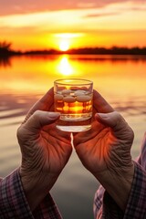 Poster - A person is holding a glass of alcohol in front of a beautiful sunset. This image can be used to depict relaxation, celebration, or enjoying a drink outdoors