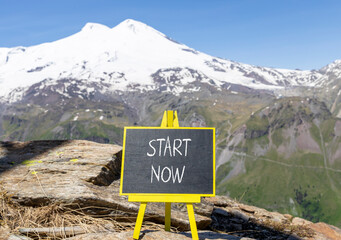 Wall Mural - Start now symbol. Concept words Start now on beautiful black chalk blackboard. Beautiful mountain Elbrus blue sky background. Business marketing, motivational start now concept. Copy space.