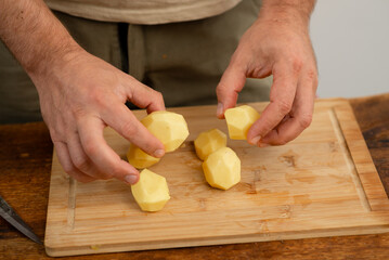 Wall Mural - Male hands hold peeled raw potatoes on a wooden cutting board, preparing for cooking
