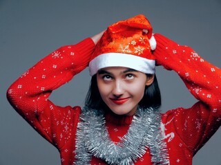 young white brunette with a bob haircut and a red New Year's hat and a red sweater with shiny silver New Year's decorative elements on her neck on a gray background