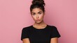 Serious displeased Latin woman with hair bun raises eyebrows looks attentively at camera purses lips has dimple on cheek dressed in casual black t shirt and jeans isolated over pink