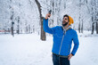 © Dorde - Excited young man using mobile phone, having video call or taking selfie while standing in public park on snowy cold winter day.