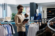 © DC Studio - Department mall employee managing inventory with digital tablet, examining and organizing apparel. Clothing store young man worker checking merchandise in stock while working