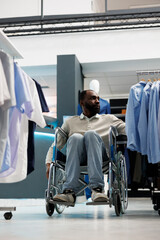 Wall Mural - Clothing store customer with physical disability choosing formal shirt and exploring apparel rack. African american man in wheelchair shopping for outfit in menswear boutique