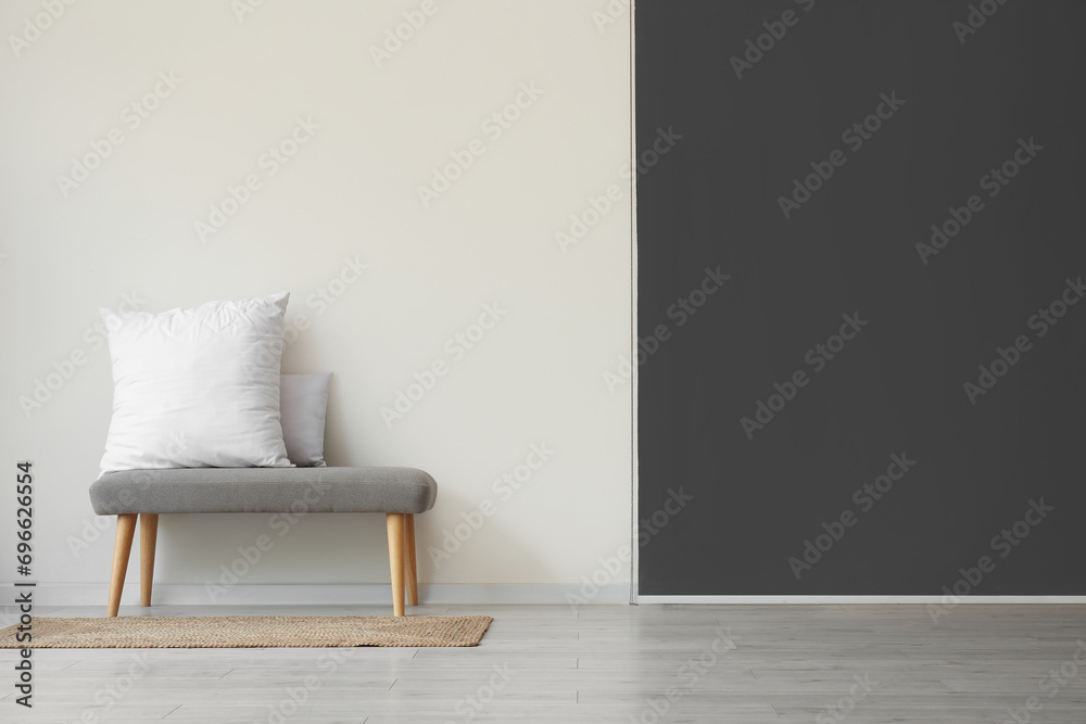 Grey bench with pillows near white wall