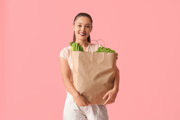 Poster - Young Asian woman with shopping bag full of fresh food on pink background