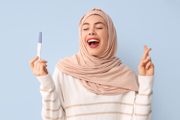 Beautiful Muslim woman with pregnancy test on blue background