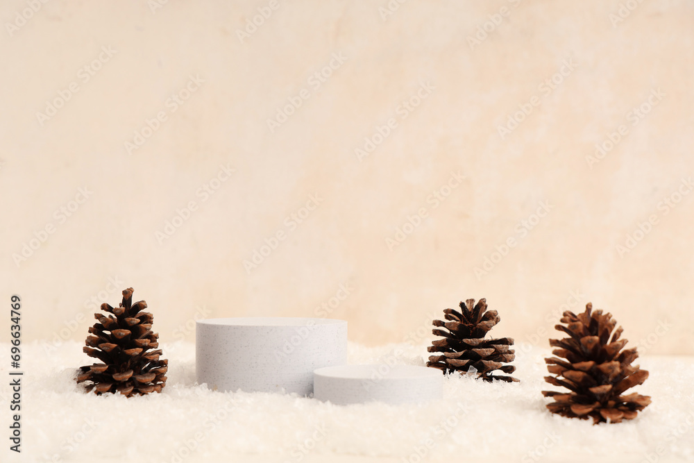 Decorative snow, plaster podiums and pine cones on beige background