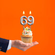 The hand that delivers cupcake with the number 69 candle - Birthday on orange background