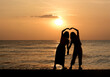 Silhouette lovely Asian women couple standing by the sea with beautiful sunset sea and sky background. Back of happy LGBTQ or friends holding hands enjoying  and relaxing on tropical summer vacation.