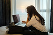 © shine - Asian woman packing suitcase on bed prepare for her travel and planning vacation travel with laptop, reading tourist blog online, booking tickets or hotel room on web getting ready for abroad journey.
