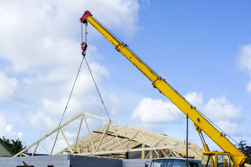 Mobile crane with yellow telescopic boom has lifted the wooden roof truss of the new building
