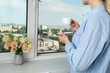 © Atlas - A woman drinks coffee near an open window with a view of the city