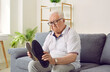 Senior man with dementia holding different shoes in his hands. Old elderly person suffering from Alzheimer's disease sitting on sofa at home alone sad and upset. Mental disorders concept.