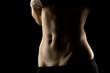 © vladimirfloyd - Close-up of a fit woman's stomach under the glow of light in a dark background