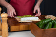 Close up of sushi chef hands making Japanese food. Man cooking sushi at restaurant or at home. Traditional asian rolls on cutting board. Maki sushi with cheese and vegetables: pepper and avocado