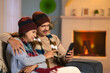 Happy couples with winter wear using mobile phone on sofa at home - concept of technology, relationship bonding and affection
