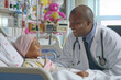 An African American pediatric oncologist empathizes with a girl sick with cancer lying in a hospital bed.