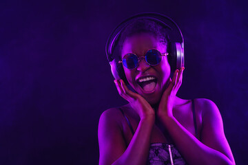 Wall Mural - Portrait of fashion young girl in cool sunglasses and with headphones in red and blue neon light in the studio.