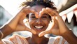 © Malynka - Close up image of smiling woman in swimwear on the beach making a heart shape with hands , Pretty joyful hispanic woman laughing at camera outside , Healthy lifestyle, self love and body care.
