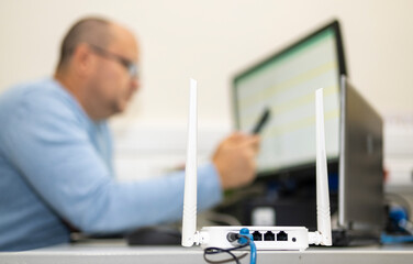 Wi-Fi router installed on a desktop in the office. In the background you can see a man working at a computer.