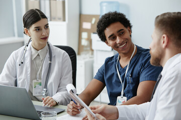 Wall Mural - Multiethnic group of smiling young doctors working together at desk in clinic