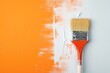 Closeup of a designer painting an orange wall with a brush.