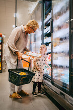 Senior Woman Holding Basket While Buying Groceries With Granddaughter At Store