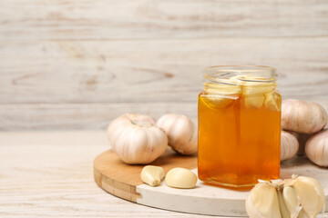 Wall Mural - Honey with garlic in glass jar on light wooden table. Space for text