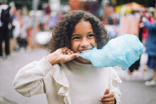 Thoughtful Girl Eating Blue Cotton Candy At Amusement Park