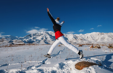 Wall Mural - Young happy woman jumping on mountains background in winter season