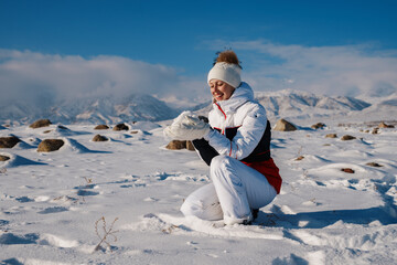 Wall Mural - Happy young woman tourist holding snow in her hands on mountains background in winter