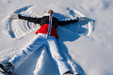 Wall Mural - Happy young woman lying on a snow and doing angel print on snow