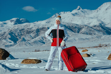 Wall Mural - Young woman tourist with red suitcase on winter mountains background