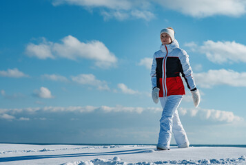 Wall Mural - Young woman in a tracksuit walking on sky background in winter