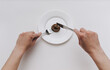 Two female hands hold a stainless steel knife and fork near the plate and cut artificial feces. Fake news, jokes. Concept of inept chef, lousy restaurant, bad food, crappy taste.