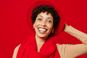 Wall Mural - Close up young smiling happy cheerful fun cool woman of African American ethnicity she wears beige sweater hat scarf looking camera isolated on plain red background studio portrait. Lifestyle concept.