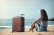 a woman sitting on the beach with a travel suitcase