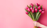 Fototapeta Tulipany - Women's Day tulip background, free space for text. Hand presents a vibrant bouquet of pink tulips against a soft pink background, evoking spring freshness